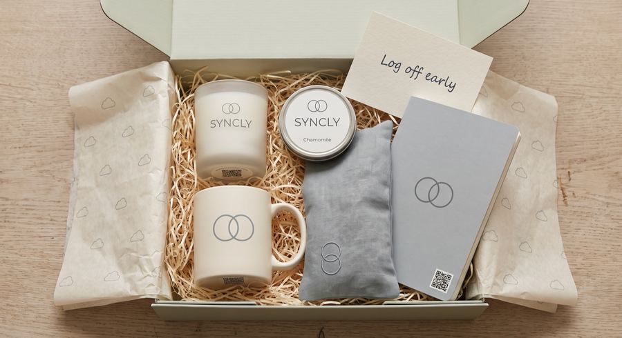 An open box of branded mugs, a candle and a notebook