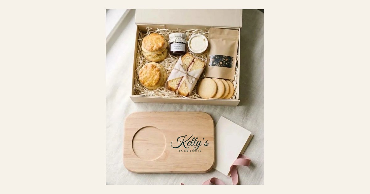 An afternoon tea gift box with scones, jam, cream, tea and biscuits, above a wooden board printed with Kelly's Tea and Biscuits